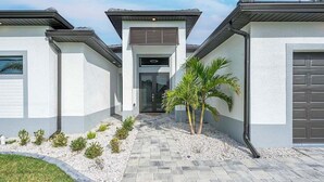 A modern two-story house with a central entrance, a garage on the right, and a pathway leading to the entrance. - Paradiso - Modern Style Vacation Villa (Cape Coral)