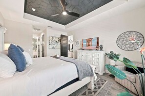 Un dormitorio con cama, cómoda, televisor y ventilador de techo.