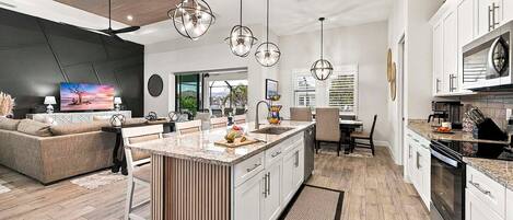 Una cocina moderna con una isla central, armarios blancos y una zona de comedor con sofá y sillas.