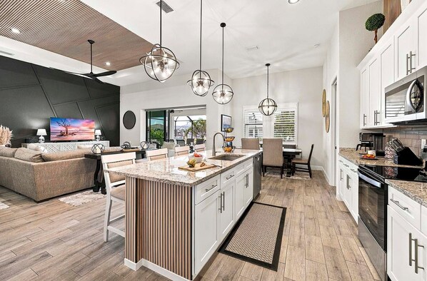 A modern kitchen with a central island, white cabinetry, and a dining area with a sofa and chairs.