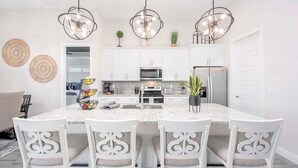 A modern kitchen with white cabinetry, a granite countertop, and a central island with seating. There are pendant lights above the island and a microwave on the countertop.