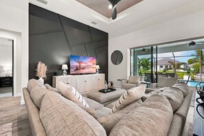 A modern living room with a sectional sofa, a flat-screen TV, and a view of a swimming pool.