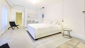 A modern bedroom with a large bed, a small round table, and a chair. - 5 Star Villa Magnolia – Luxury Lakefront Retreat (Algarve)