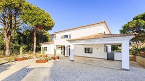 A modern two-story house with a tiled roof, a paved driveway, and a garden with cacti and other plants. - 5 Star Villa Magnolia – Luxury Lakefront Retreat (Algarve)