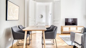 Un salon moderne avec une table à manger en bois, quatre fauteuils gris, un téléviseur et un grand tableau abstrait.