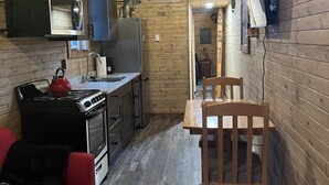 A compact kitchen with wooden walls, a stove, a microwave, and a sink. There is a red sofa and a wooden table with chairs. - Osprey Lake Caboose beside the Kettle Valley Railway and 2 mins from Osprey Lake (Summerland)