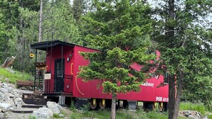 A red caboose with a small porch and a bench, surrounded by rocks and trees. - Osprey Lake Caboose beside the Kettle Valley Railway and 2 mins from Osprey Lake (Summerland)