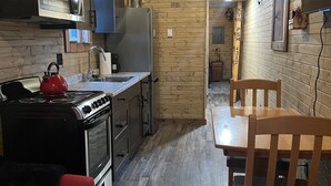 A compact kitchen with a stove, microwave, and refrigerator. There is a wooden dining table with chairs and a red sofa. - Osprey Lake Caboose beside the Kettle Valley Railway and 2 mins from Osprey Lake (Summerland)
