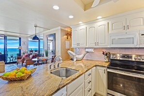 A kitchen with white cabinets, a granite countertop, a stainless steel sink, and a built-in microwave.