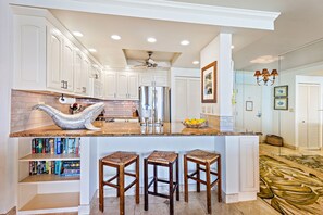 A modern kitchen with white cabinetry, a large island with bar stools, and a ceiling fan.