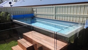 A swimming pool with glass sides, wooden steps, and a hot tub.