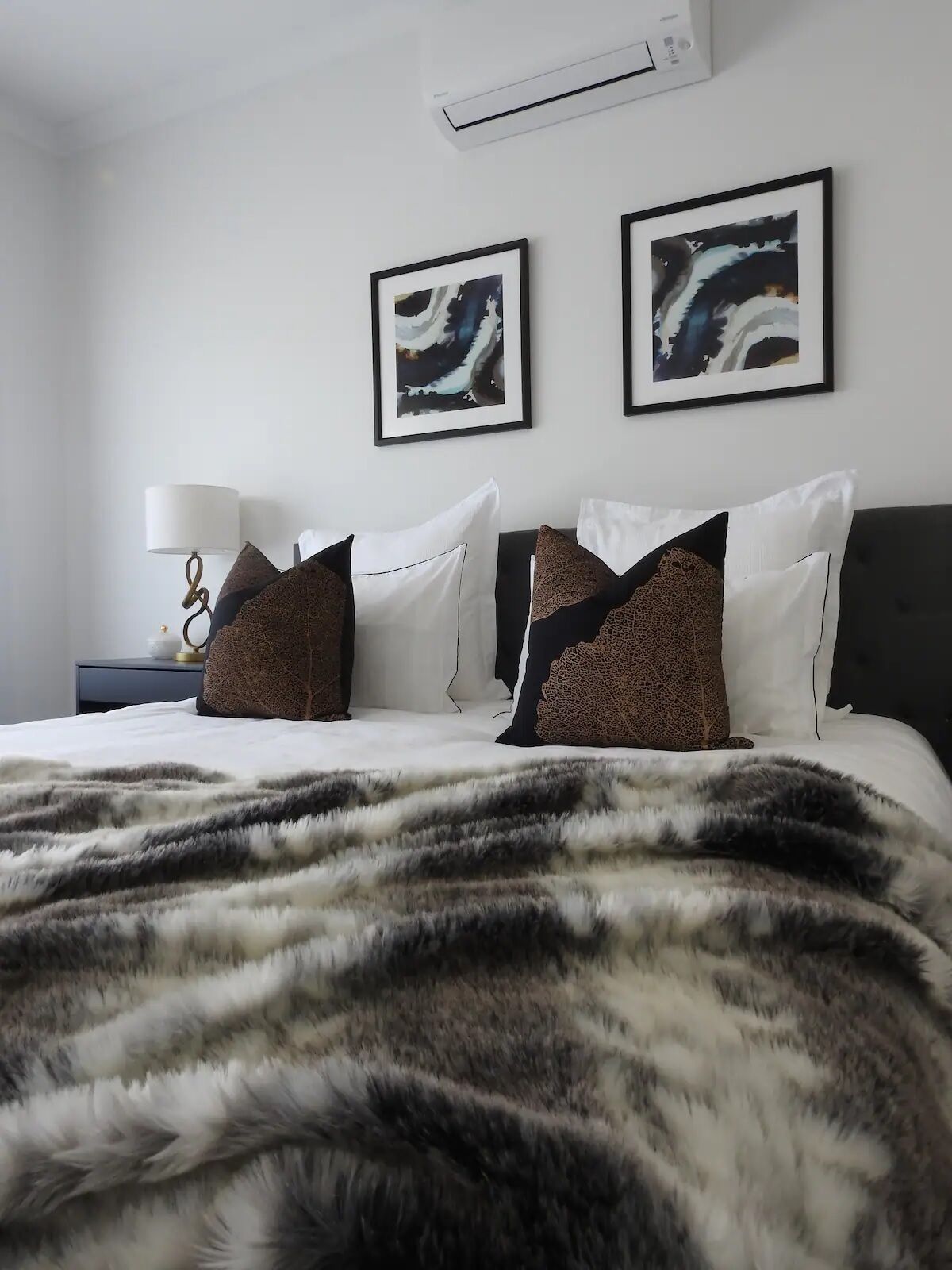 Een netjes opgemaakt bed met een bedsprei met patroon, een bedlampje en twee ingelijste kunstwerken aan de muur.