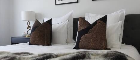 Een netjes opgemaakt bed met een bedsprei met patroon, een bedlampje en twee ingelijste kunstwerken aan de muur.