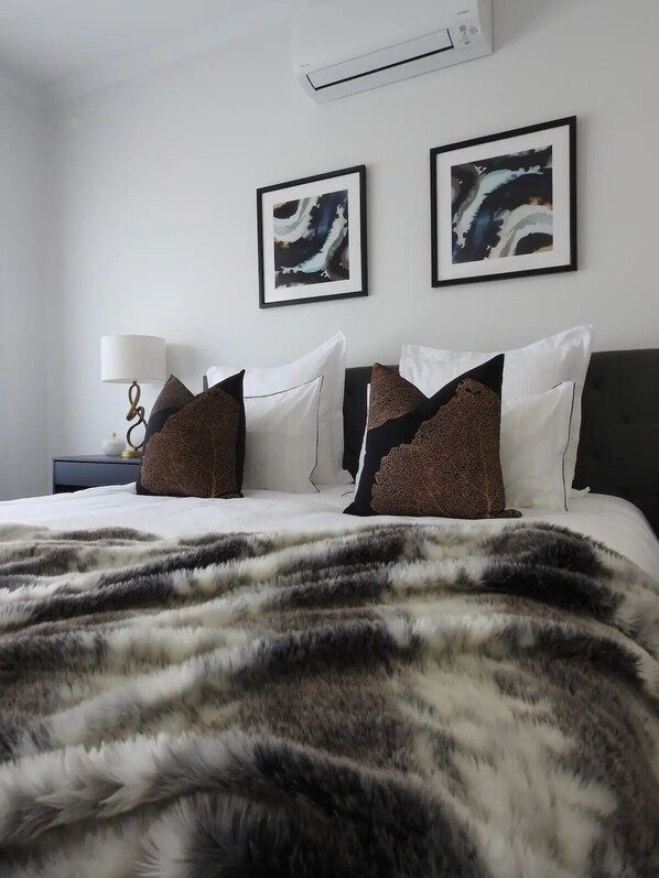 A neatly made bed with a patterned blanket, a bedside lamp, and two framed artworks on the wall.