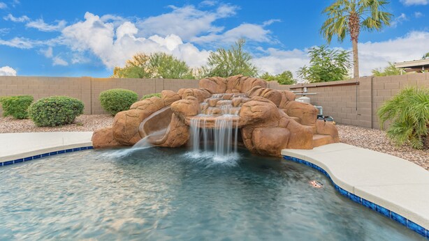 A pool with a waterfall feature surrounded by rock formations and palm trees.
