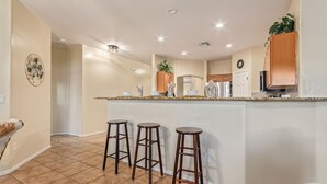 A kitchen with a central island, three bar stools, and wooden cabinets.