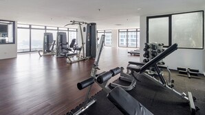 Un gimnasio espacioso con diverso equipo de ejercicio, ventanas amplias y un techo alto.