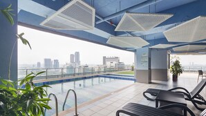 Un área de piscina en la azotea con vista a la ciudad, sillas de descanso y plantas en macetas.