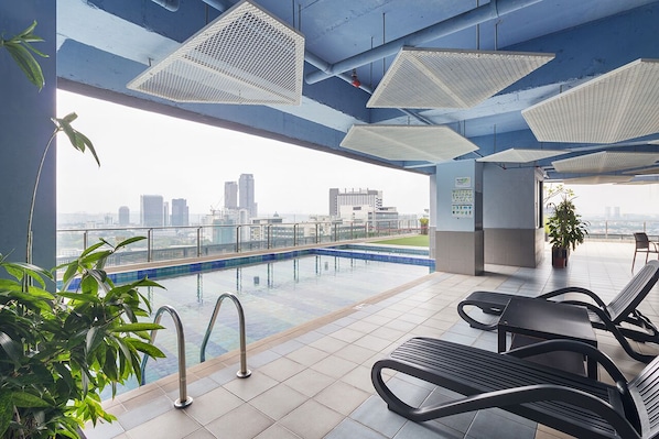 A rooftop pool area with a city view, lounge chairs, and potted plants.