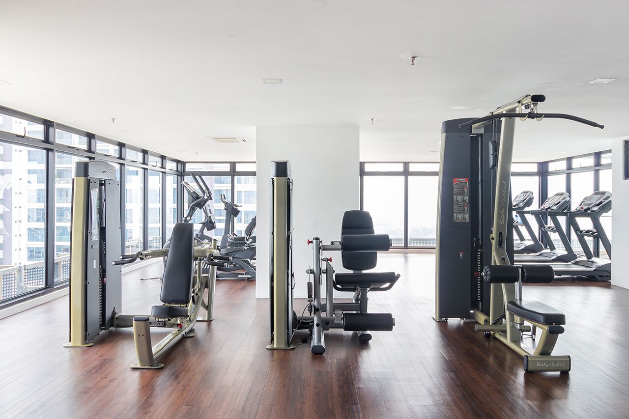 Ein Fitnessstudio mit verschiedenen Trainingsgeräten, großen Fenstern und Blick auf Gebäude.