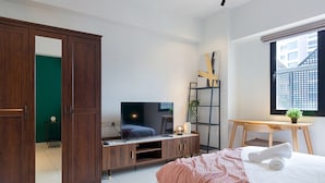 Un dormitorio moderno con cama, televisión, armario, escritorio y ventana.