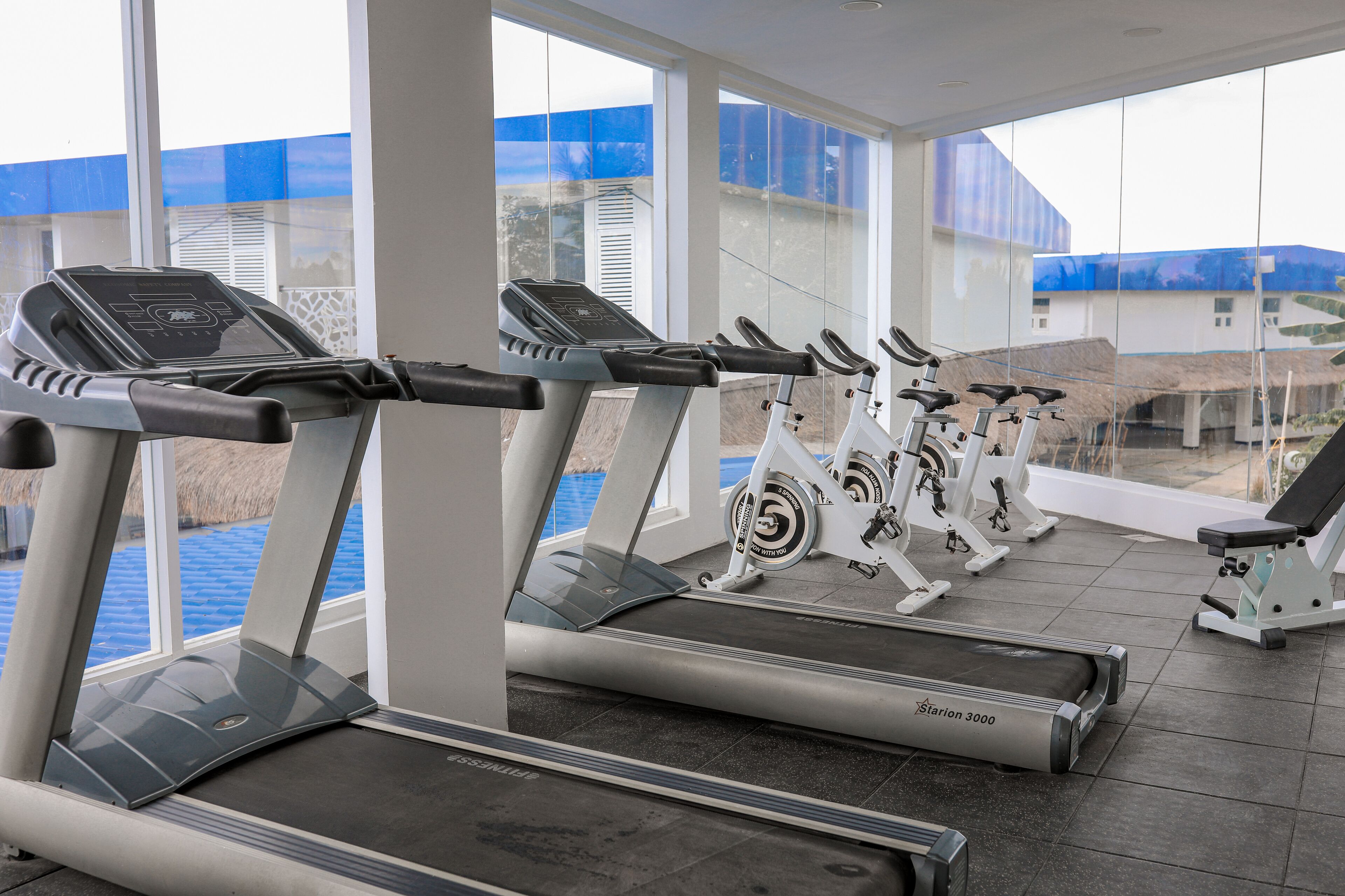 A gym with treadmills and stationary bikes, large windows, and a view of buildings outside.