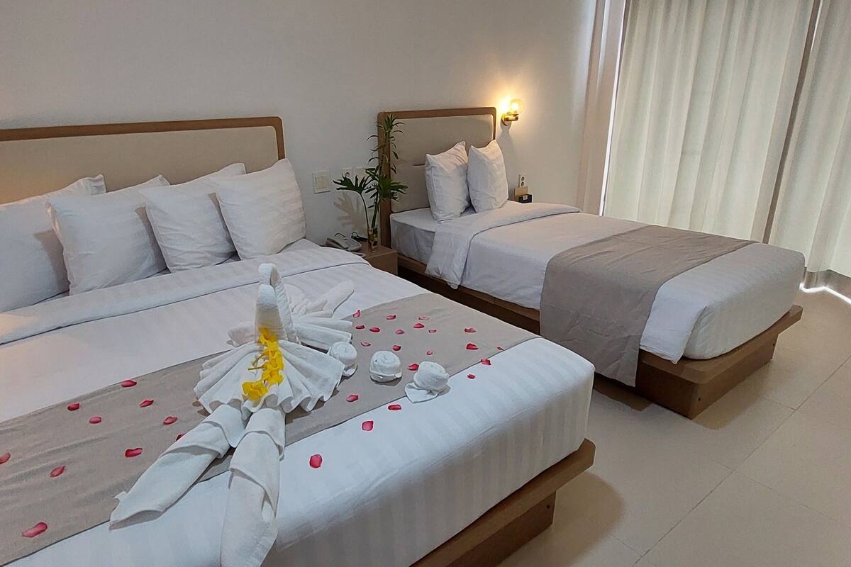 Une chambre d’hôtel avec deux lits, chacun agrémenté de draps et d’oreillers blancs. Des serviettes décoratives et des pétales de rose sont disposés sur les lits.