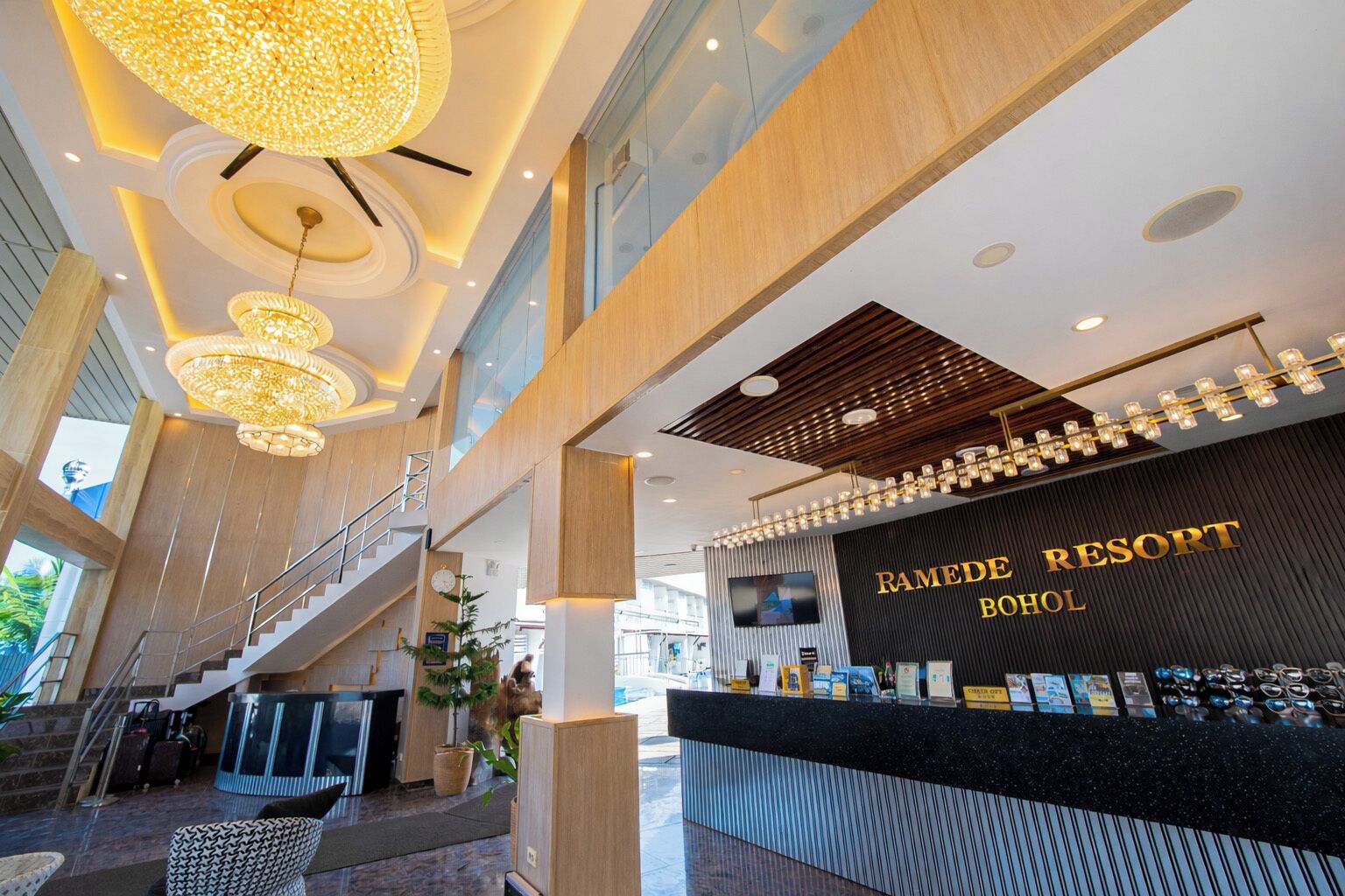 A hotel lobby with a reception desk, a staircase, and a large chandelier.