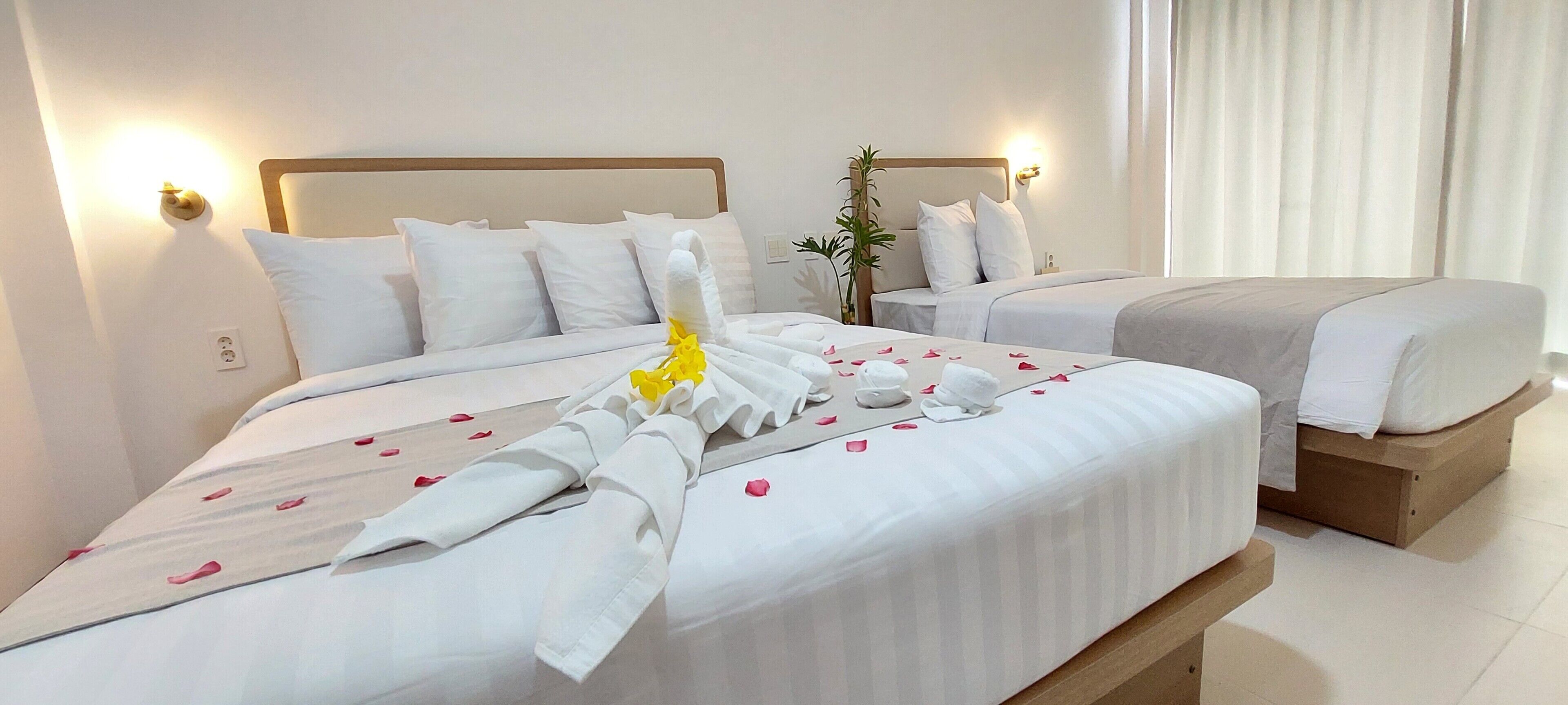 A hotel room with two beds, each with white linens and pillows, a bedside plant, and a wooden bench.