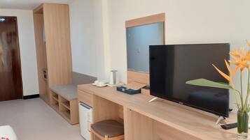 Habitación de hotel compacta con escritorio de madera, televisor de pantalla plana, una pequeña zona de estar y un jarrón con una sola flor.