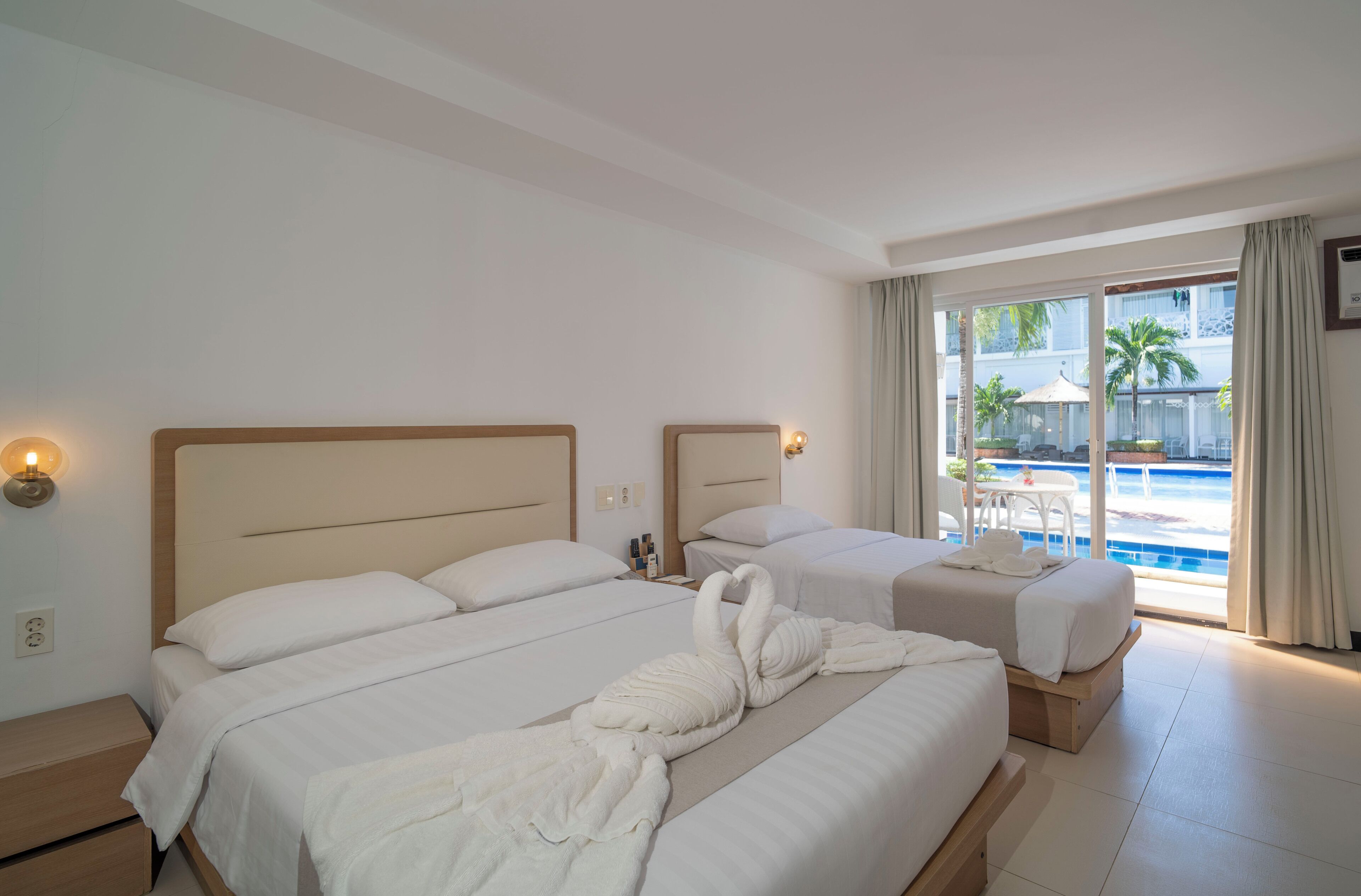 A hotel room with two beds, a view of a swimming pool, and a balcony with outdoor furniture.