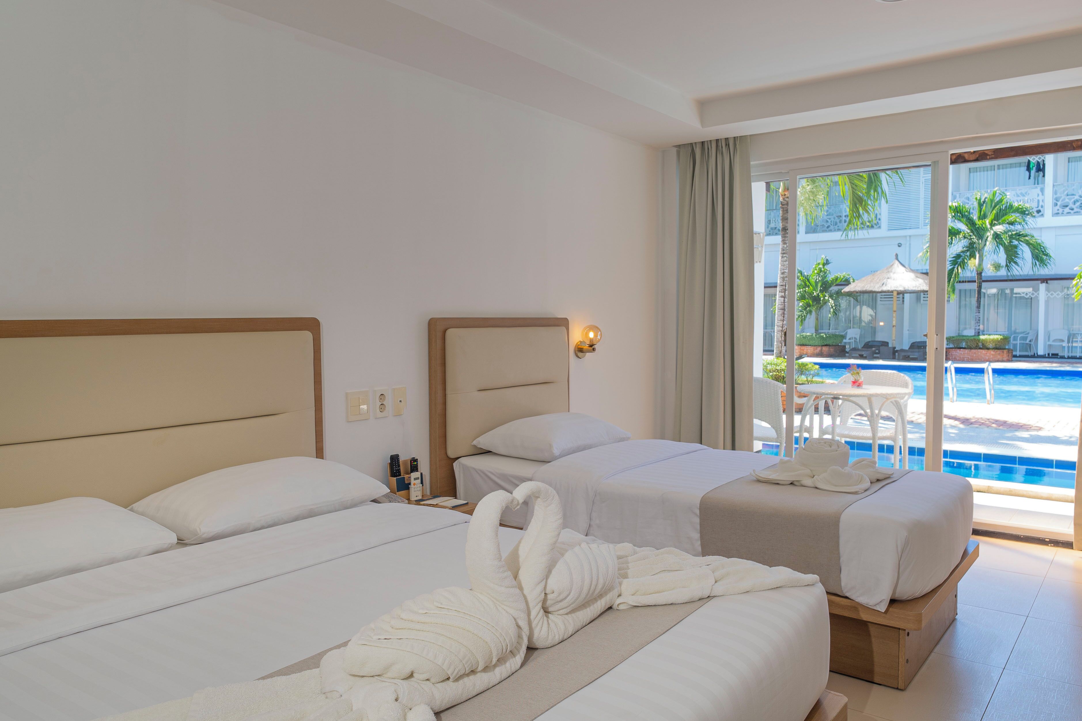 A hotel room with two beds, a view of a swimming pool, and a balcony with outdoor furniture.