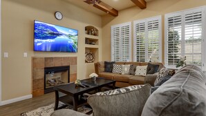 A living room with a flat-screen TV, a fireplace, a sofa, and a ceiling fan. - Single story Luxurious 1 BR 1 BA Kitchen Living Resort Pools Gym (La Quinta)