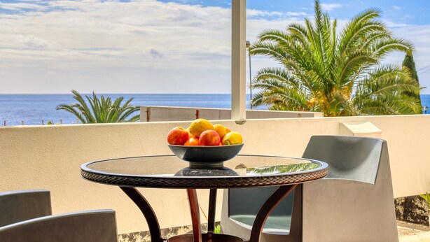 Un tavolo rotondo in vetro con una ciotola di frutta su un balcone vista mare.