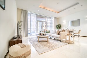 A modern living room with a sofa, coffee table, and chairs, large windows, and a dining area.