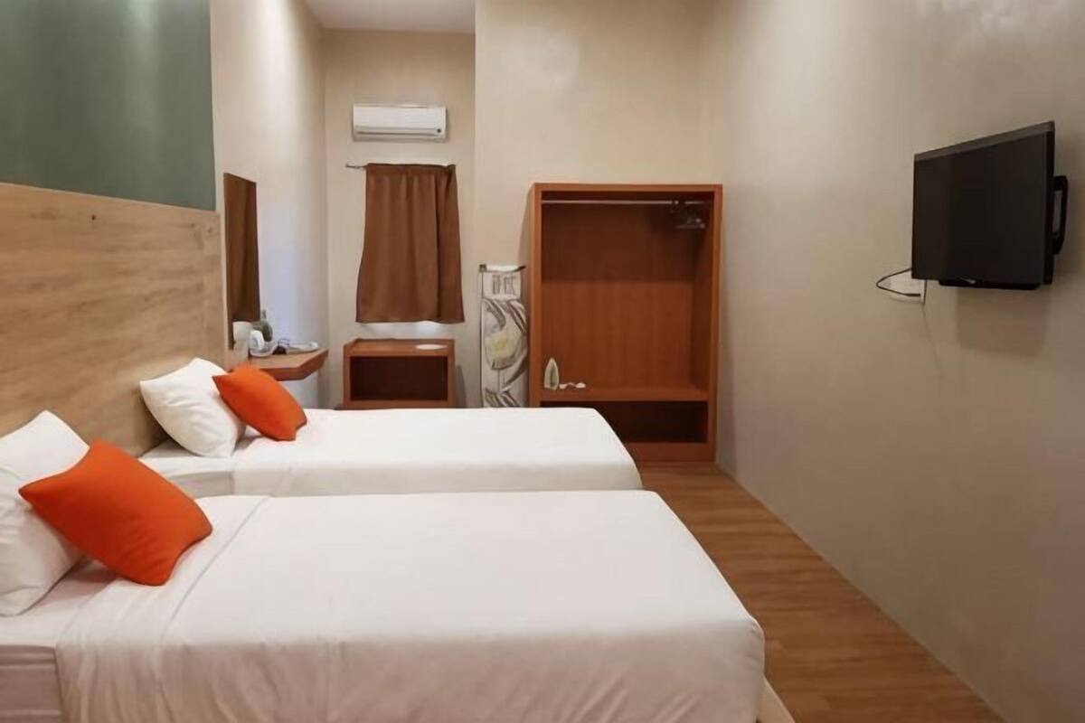 Ein Hotelzimmer mit zwei Betten, einem Fernseher, einer Dusche und einem kleinen Tisch mit einem Stuhl.