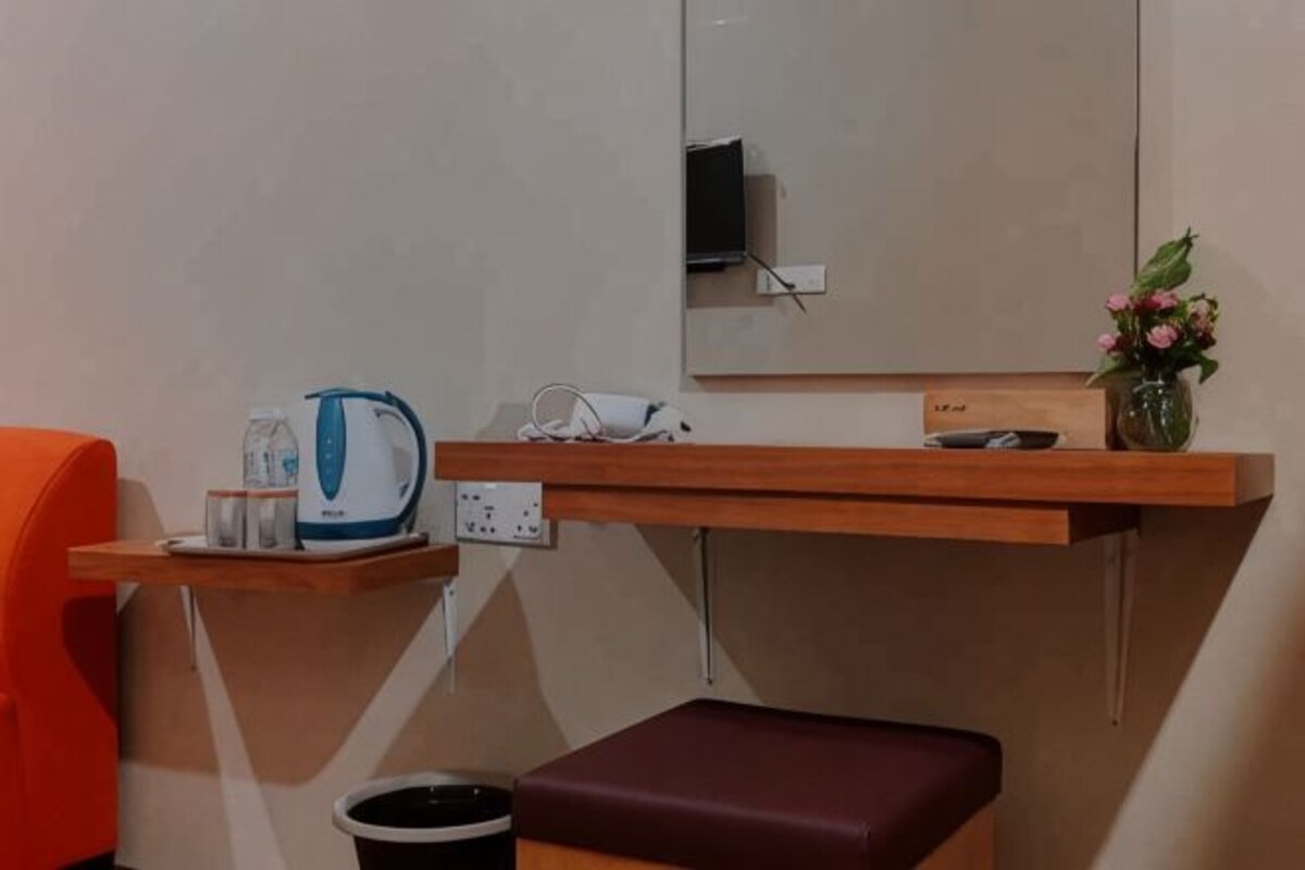 A hotel room with a wooden shelf holding a kettle, a vase with flowers, and a small table.