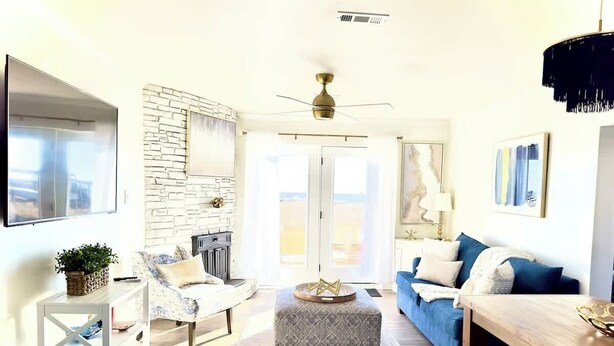 Una sala moderna con pared de piedra, chimenea, ventilador de techo y comedor con mesa y sillas de madera.