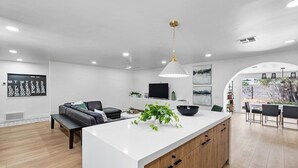 A modern kitchen with a central island, a dining area with a table and chairs, a living room with a sofa, and a TV mounted on the wall. - NEW 1 Min Walk DT Gilbert - 4 Bedroom Retreat (Gilbert)