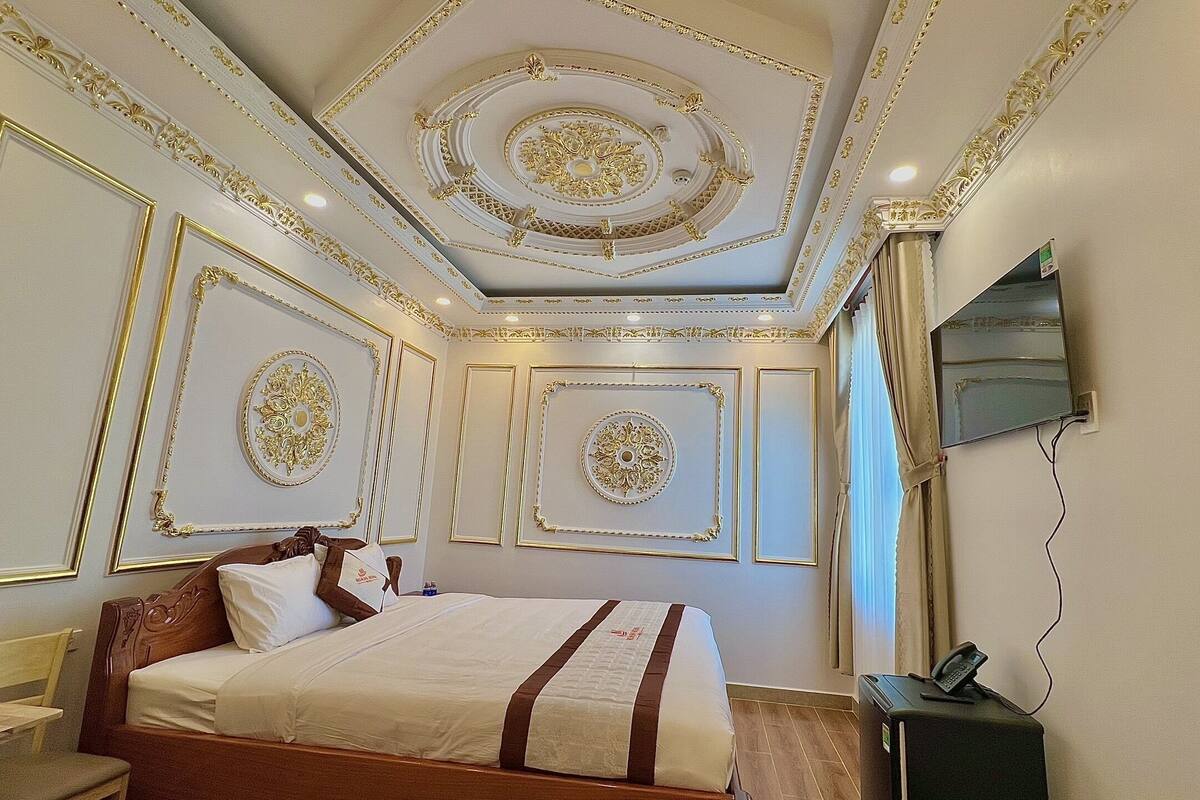 A hotel room with a bed, a desk, a chair, a TV, and a telephone.