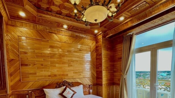 Une chambre aux murs lambrissés, avec un grand lit, un lustre et une vue par la fenêtre.