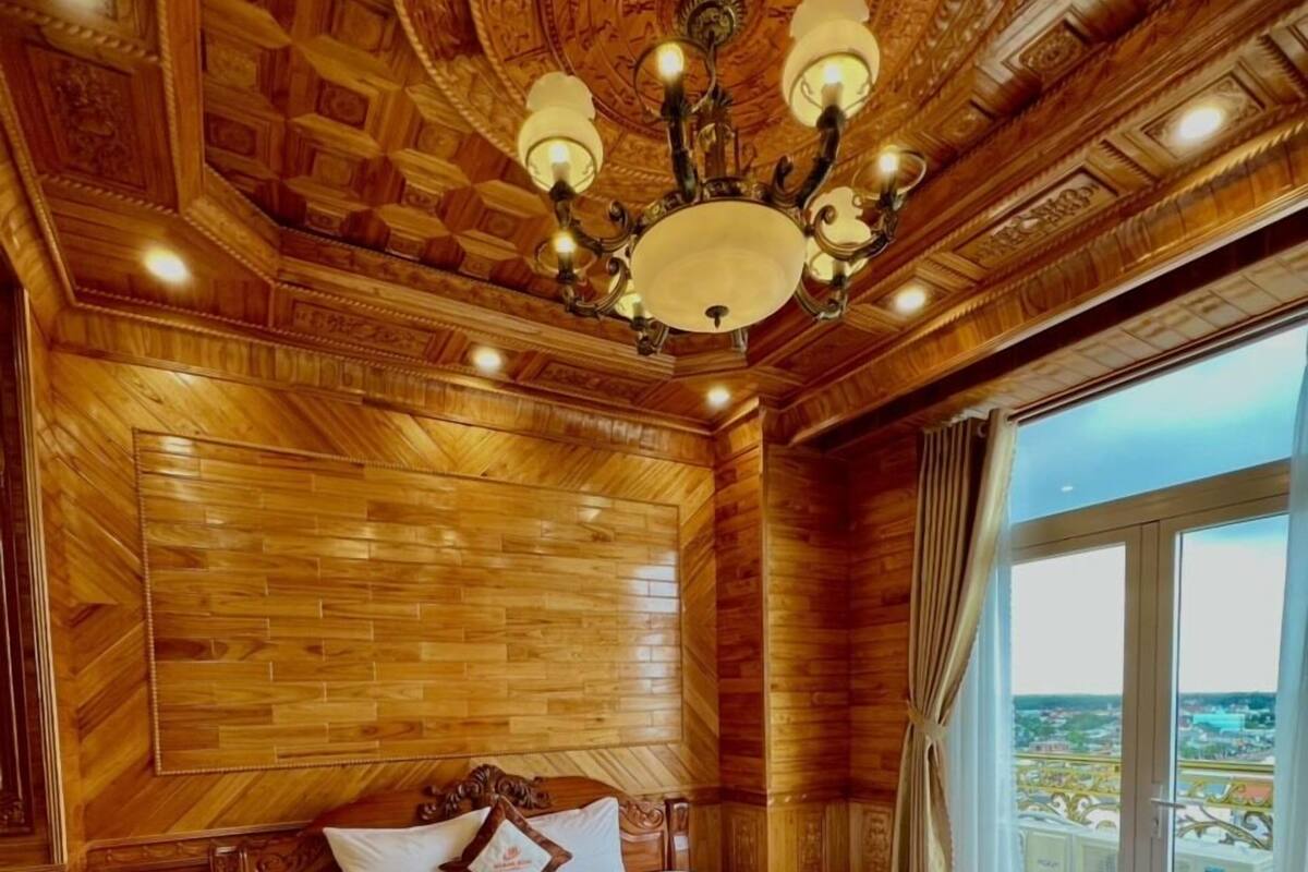 A wooden-paneled bedroom with a large bed, a chandelier, and a view through a window.