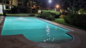 A swimming pool at night with surrounding greenery and a building in the background. - luxury 3 rooms   pool caampo de golf (Punta Cana)