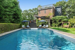 Relax by the pool surrounded by lush greenery and a wooden deck.