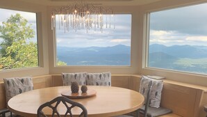 Une table de salle à manger ronde, entourée de chaises, un lustre et une vue sur les montagnes par de grandes fenêtres.