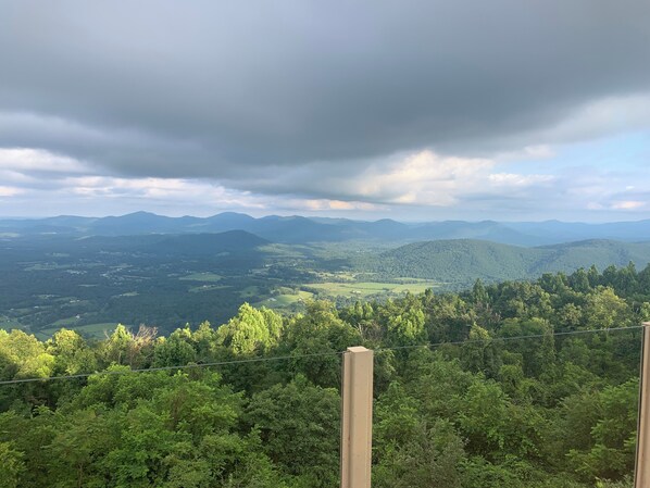 A panoramic view of a mountainous landscape with a forested foreground and distant hills under a cloudy sky.