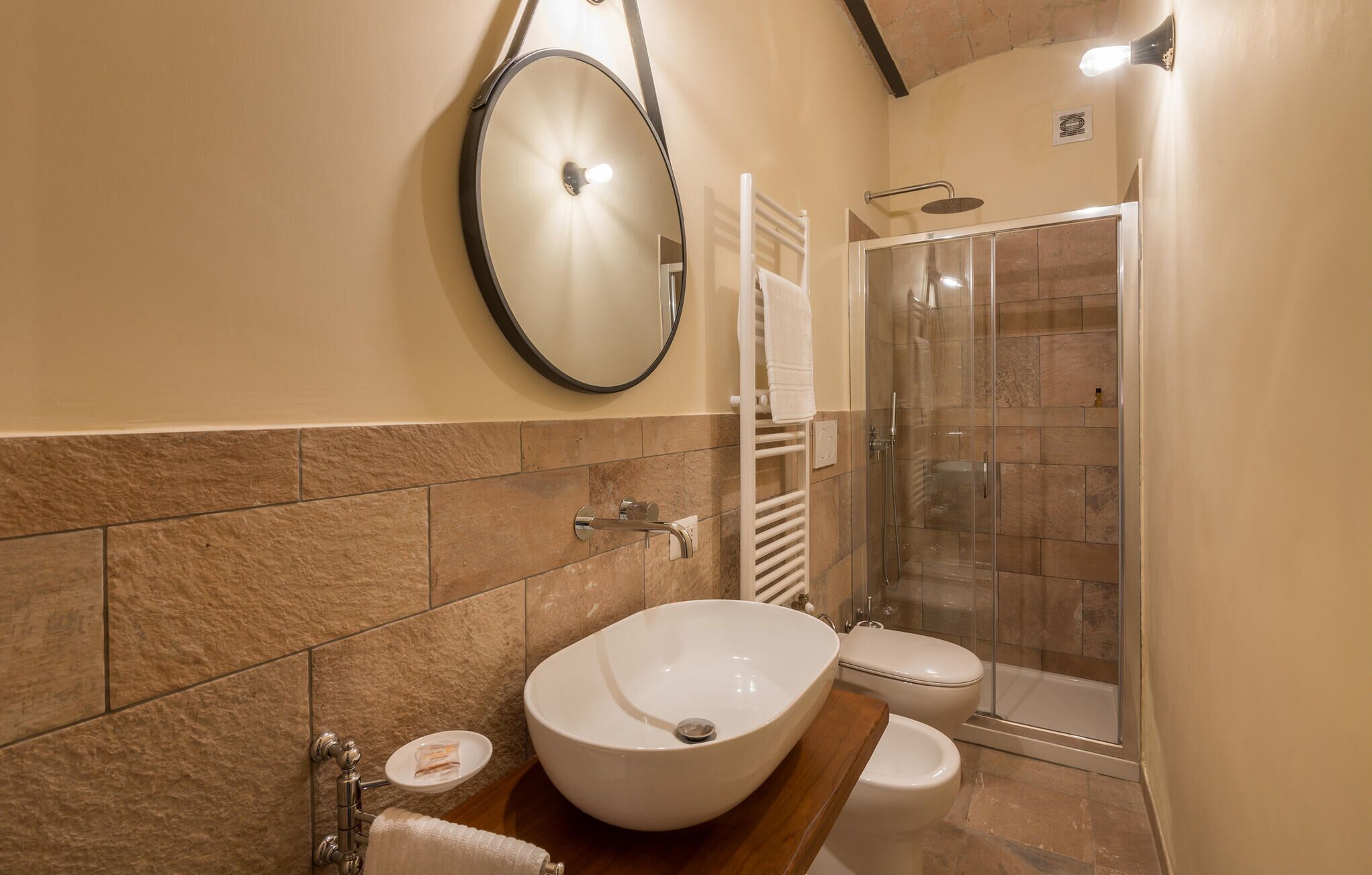 A bathroom with a large oval sink, a toilet, a glass-enclosed shower, and a towel rack.