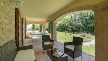 Eine überdachte Terrasse mit Korbmöbeln, einem Tischtennisschläger und Blick auf einen Garten.