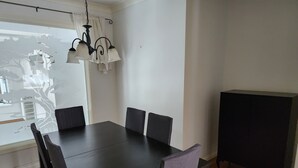 Un espace repas comprenant une table rectangulaire, six chaises, un lustre et une fenêtre ornée d’un motif représentant un arbre.