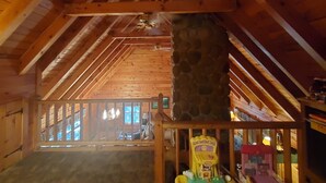 A wooden interior with a stone pillar, wooden beams, and a view of the outside.